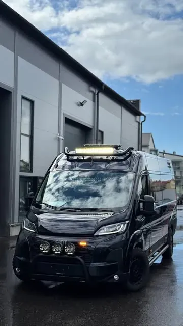 Musta Fiat Ducato lisävaloilla hallin edessä