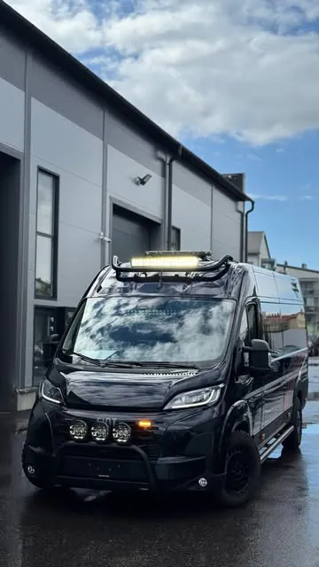 Musta Fiat Ducato -pakettiauto lisävaloineen hallin edessä
